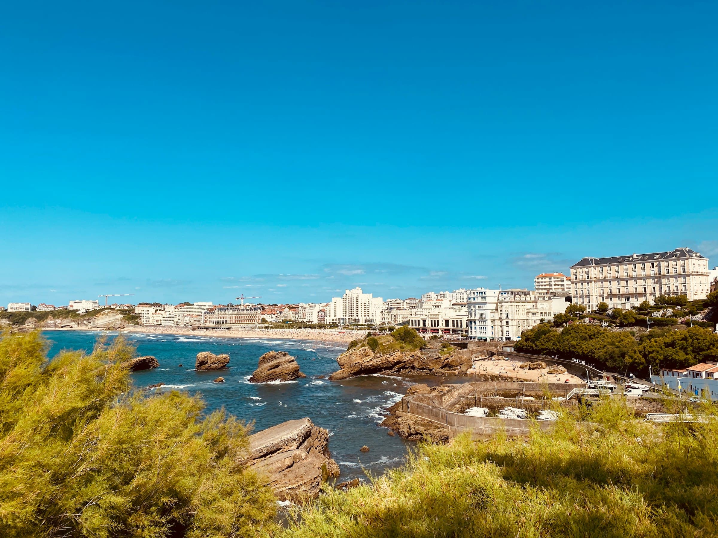La Grande Plage de Biarritz depuis les rochers, l’Hôtel du Palais au fond, sous un ciel bleu