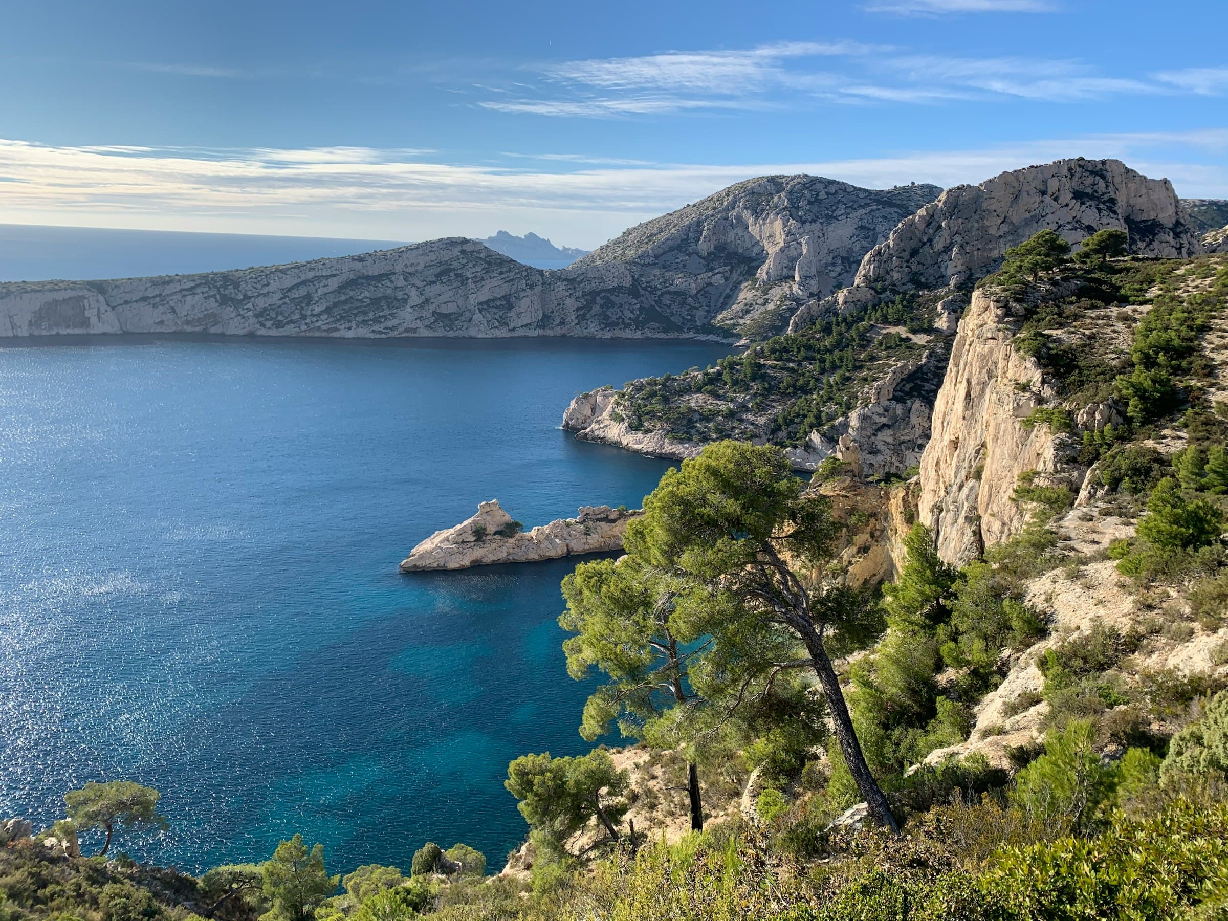 Les calanques de Marseille en plein jour, falaises calcaires couvertes de pins plongeant dans une mer d’un bleu profond