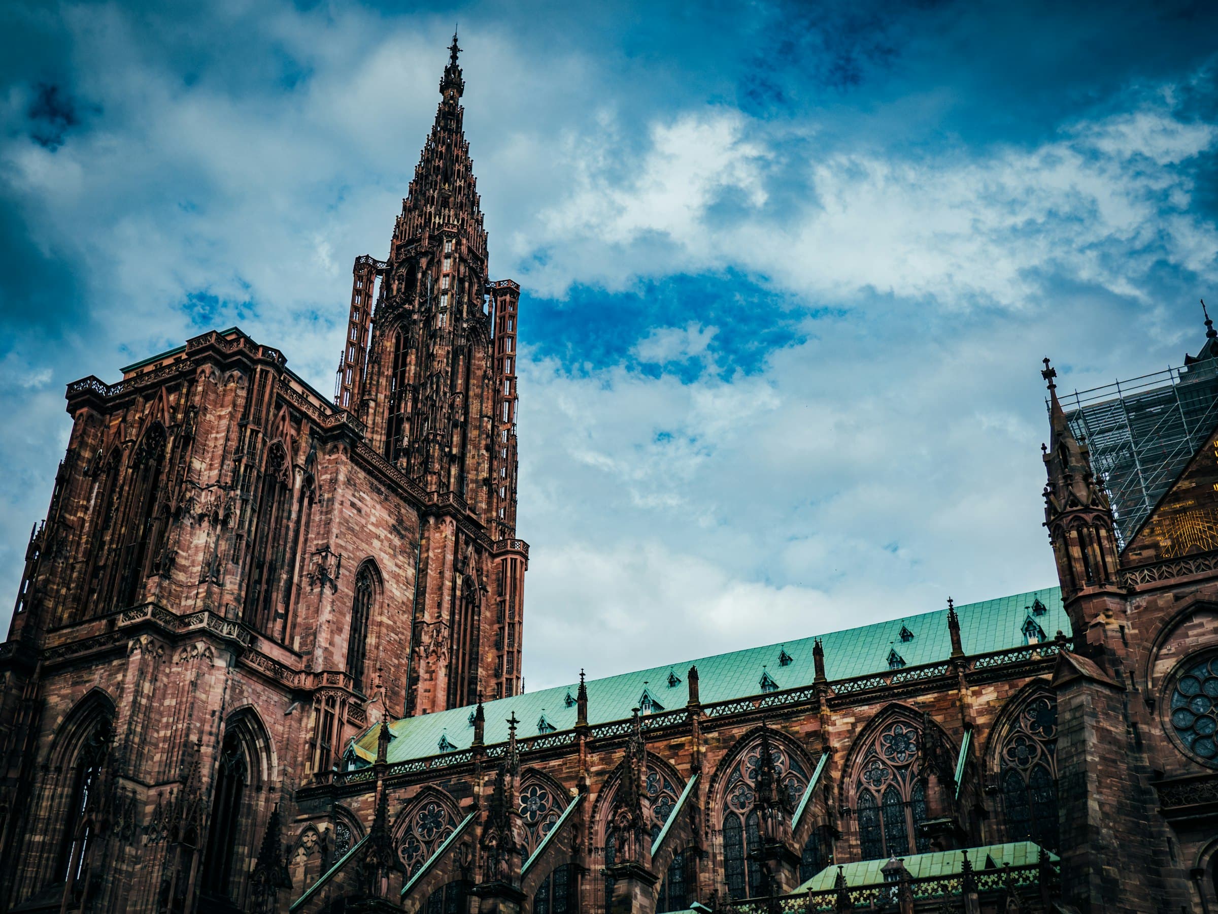 La cathédrale de Strasbourg vue de flanc, sa flèche de grès rose et sa toiture de cuivre vert sur un ciel bleu nuageux