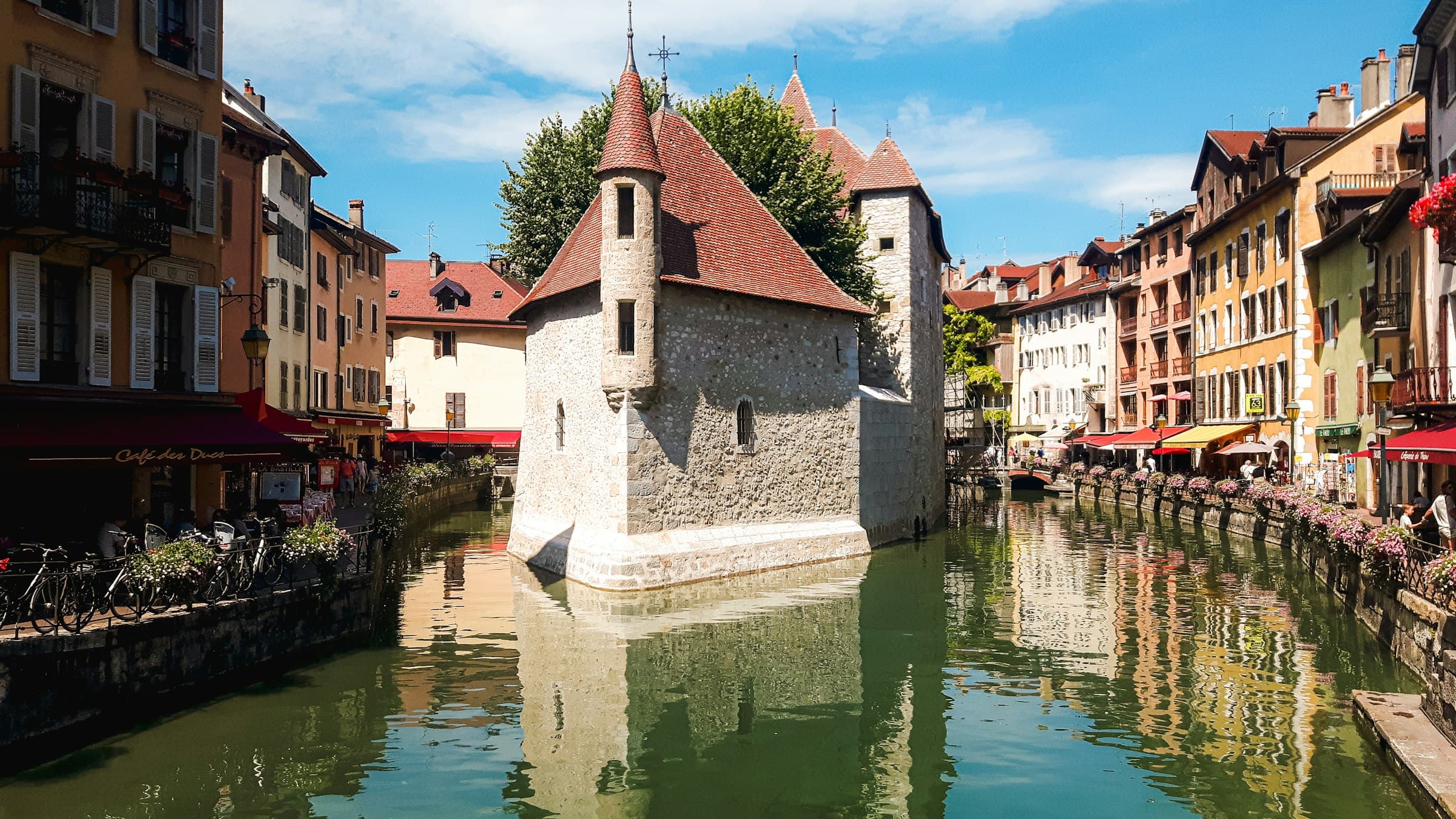 Le Palais de l’Isle au milieu du canal du Thiou, à Annecy, entre les façades colorées de la vieille ville, sous un ciel bleu