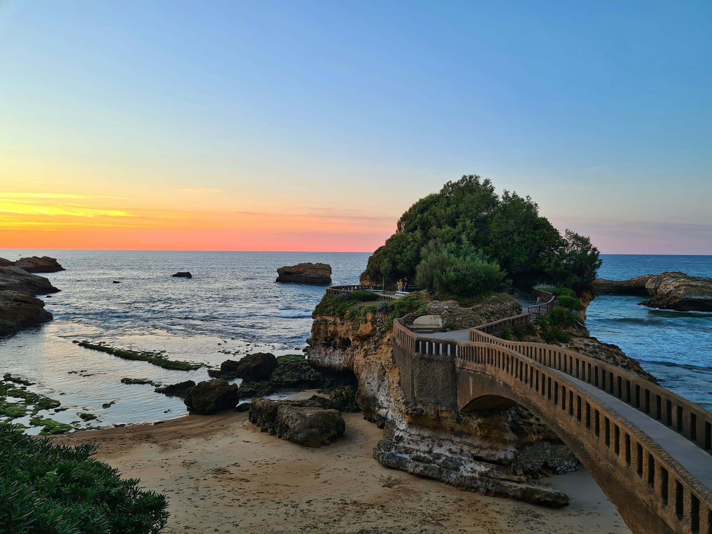 La passerelle du Rocher du Basta à Biarritz au couchant, l’océan calme et la plage de sable au premier plan