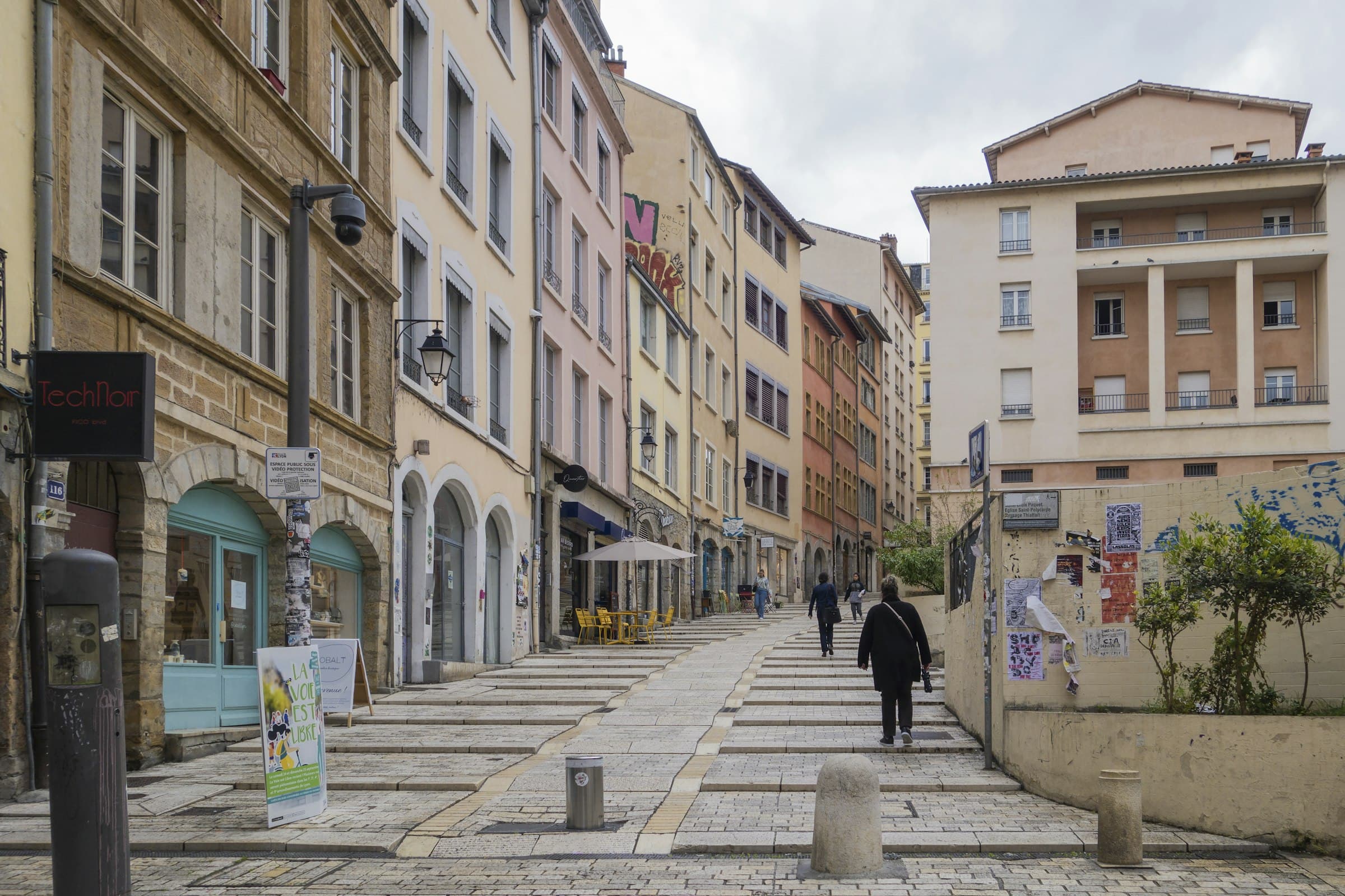 Une rue en pente de la Croix-Rousse à Lyon, escaliers et immeubles anciens de part et d’autre sous un ciel couvert